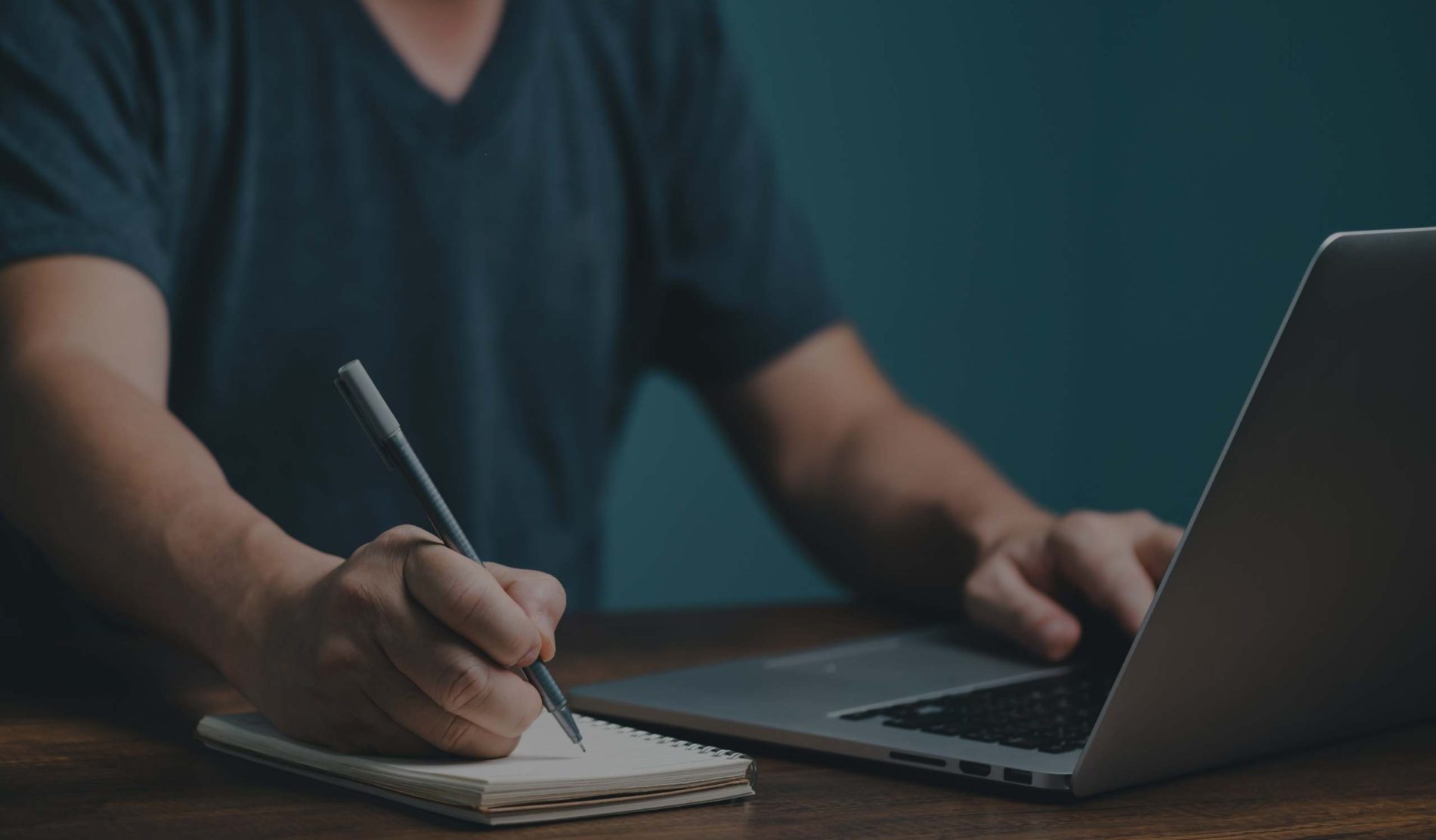 Man at a laptop with a pen and paper to signify online learning